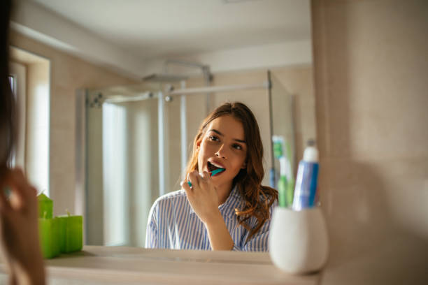 Making sure they'll stay clean all day Portrait of a beautiful young woman brushing teeth in the bathroom. woman brushing teeth mirror stock pictures, royalty-free photos & images