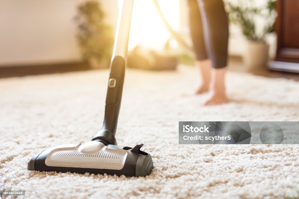 Woman using a vacuum cleaner while cleaning carpet in the house. Young woman using a vacuum cleaner while cleaning carpet in the house. Carpet - Decor Stock Photo