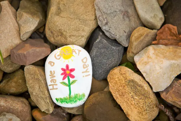 A painted "kindness stone" laying in a pile of rocks that reads "Have a nice day!"