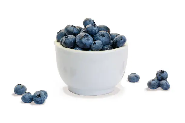 Photo of Closeup  blueberry in white ceramic cup  and small piles of blueberry on white background isolated