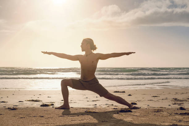 uomo che esegue esercizi di yoga su una spiaggia vicino al tramonto. - sunset yoga young men caucasian foto e immagini stock