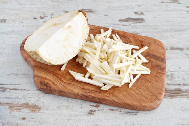 Root celery cut into small pieces with the half of the whole celery root on a olive wood cutting board on a light wooden background. Step by step cooking Root celery cut into small pieces with the half of the whole celery root on a olive wood cutting board on a light wooden background. Step by step cooking. Celeriac stock pictures, royalty-free photos & images