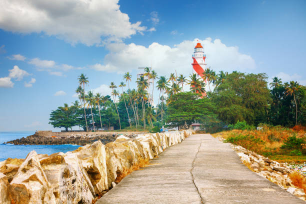 faro di thangassery sulla scogliera circondato da palme e grandi onde del mare sulla spiaggia di kollam. kerala - kollam foto e immagini stock