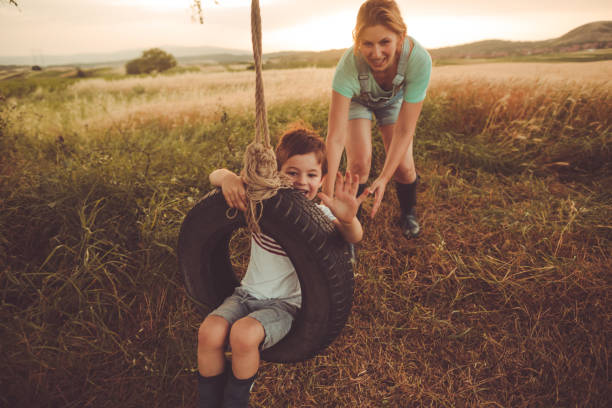 Moter and son making memories for life Photo of young mother bonding with her son, swinging him on a tire swing they have built together. They enjoy beautiful summer day, outdoors in the nature. tire swing stock pictures, royalty-free photos & images
