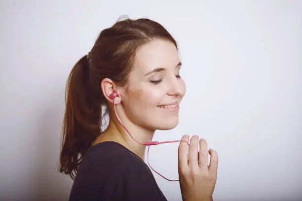 Pretty cool smiling girl listening to music with pink in-ears headphones