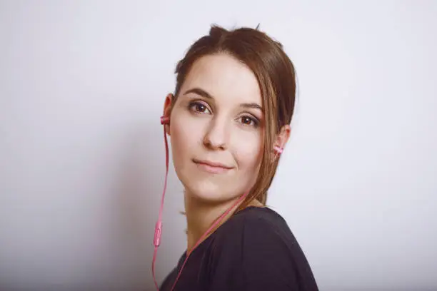 Pretty cool smiling girl listening to music with pink in-ears headphones