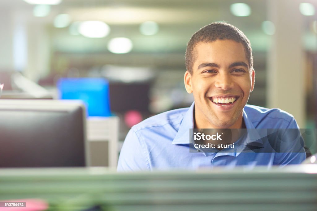 male office worker chatting to colleague a young male office worker talks to a colleague in a large open plan office . Trainee Stock Photo