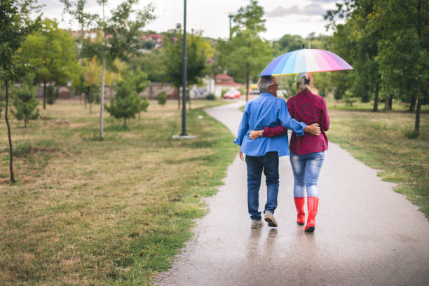 couple avec un parapluie arc-en-ciel - umbrella senior adult couple autumn photos et images de collection