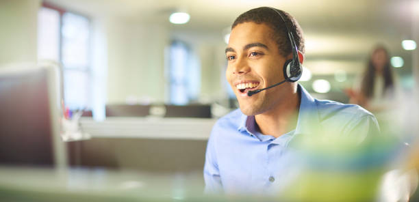 young call centre worker chatting. a young male call centre worker takes a call. liverpool one stock pictures, royalty-free photos & images