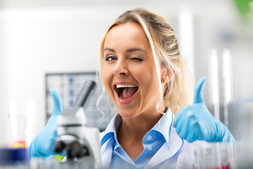 Portrait of happy young attractive laughing woman scientist showing thumbs up in the scientific chemical laboratory
