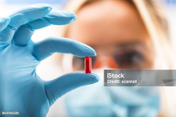 Young Attractive Female Scientist Holding A Red Transparent Pill Stock Photo - Download Image Now