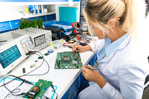 Young female digital electronic engineer testing computer PC motherboard in laboratory