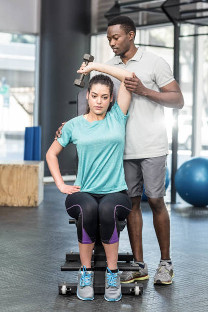 istock Athletic woman lifting weights helped by trainer 843782488