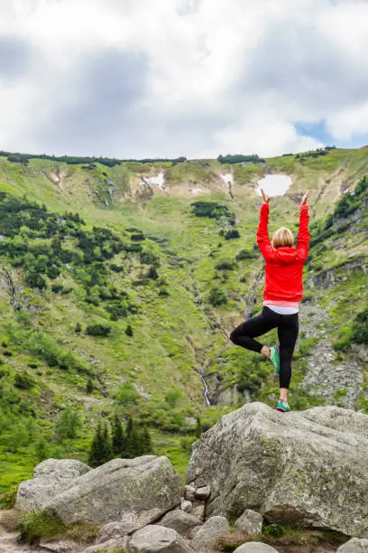 Woman meditating in yoga pose in front of mountain lake. Female hiker relaxing in beautiful inspirational mountains landscape. Healthy lifestyle outdoors in nature concept.