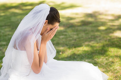Side view of a beautiful worried bride sitting at the park