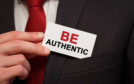 Businessman putting a card with text Be Authentic in the pocket