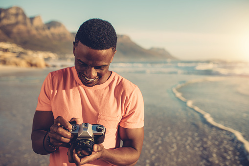 African man checking photos in his digital camera. Young man with digital photo camera standing on the beach.