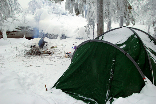 Green tent on a campsite in a winter forest near to mountains. Ural, Russia.