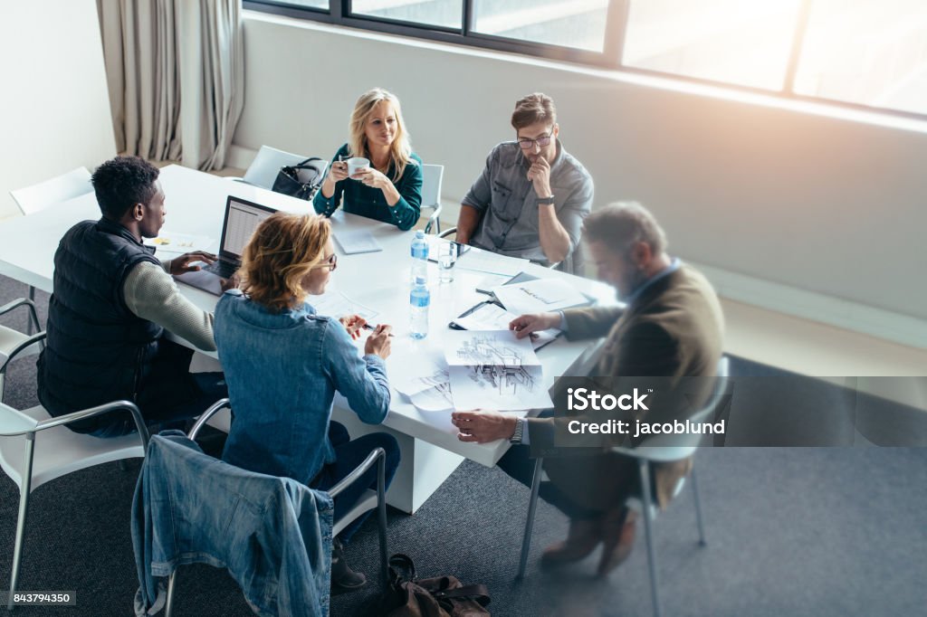 Business people discussing in meeting at office Business people working and discussing together in meeting at office. Businessman looking at building sketch with colleagues sitting around table. Casual Clothing Stock Photo
