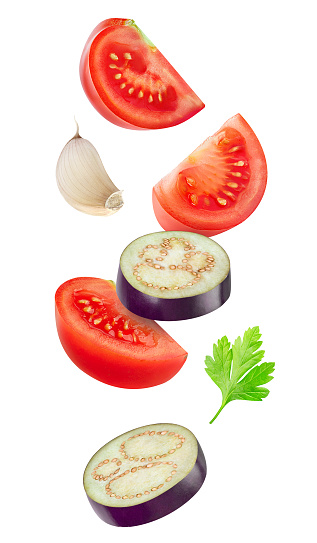 Isolated cut vegetables. Raw slices of eggplant, tomato and garlic flying in the air isolated on white background with clipping path