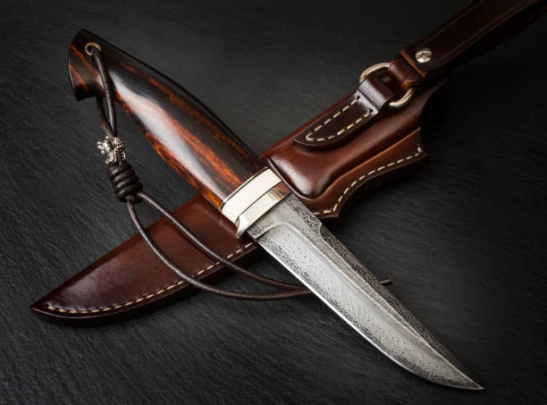 Pięknie wykonany, egzotyczny nóż z misternie zaprojektowanym ostrzem i skórzaną pochwą na ciemnej powierzchni.