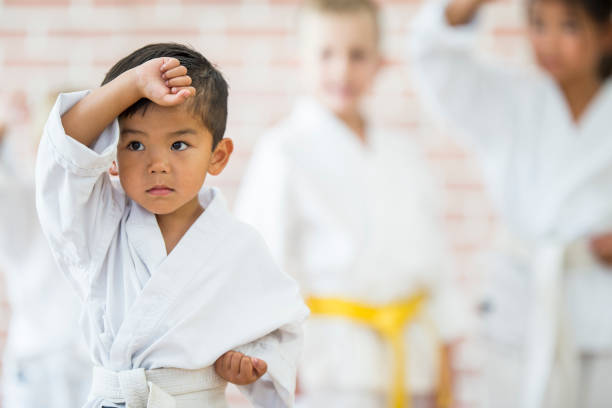 Tough Pose A multi-ethnic group of children are indoors at a martial arts studio. They are wearing karate clothing. An Asian boy is doing a pose and looking tough. martial arts stock pictures, royalty-free photos & images