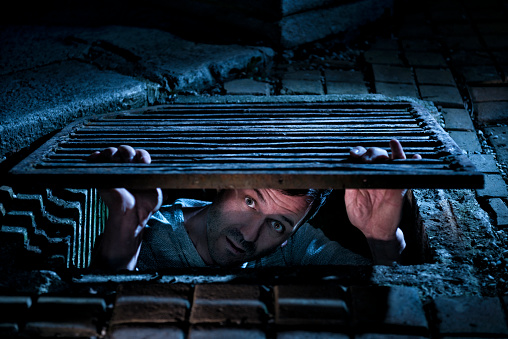 Handsome man looking scared out of a manhole at night