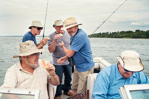 Three middle aged men are enjoying a sunny day out on the water fishing.  The water is a freshwater lake in the western part of the Great Lakes region of the United States.