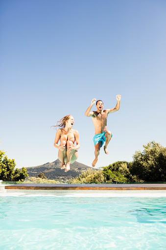 Happy couple jumping in the pool in a sunny day