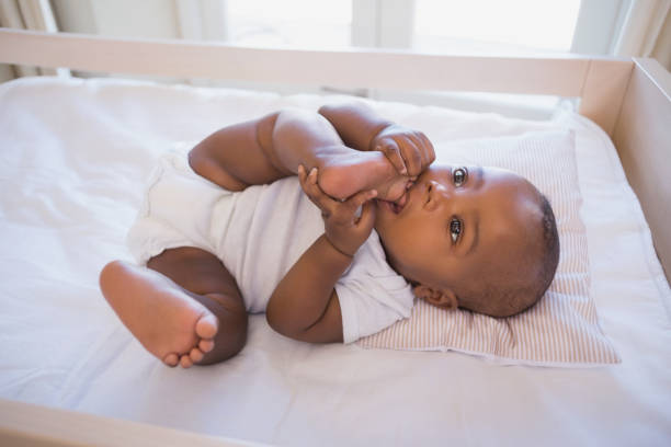 istock Adorable baby boy lying in his crib chewing foot 843870708