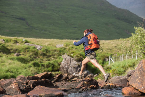 istock Athletic hiker leaping across rocks in a river 843873668