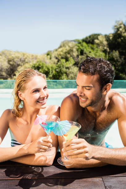 istock Happy couple leaning on pool edge and toasting with cocktails 843878258