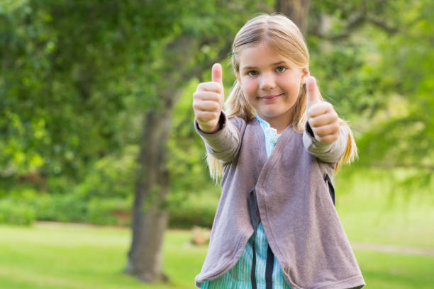 istock Cute young girl gesturing thumbs up at park 843905942