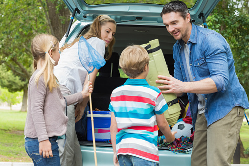 Happy family of four unloading car trunk while on picnic