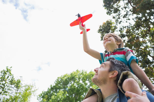 Boy with toy aeroplane sitting on fathers shoulders
