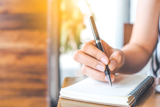 istock woman's hand is writing on a blank notepad with a pen on a wooden desk. 843930852
