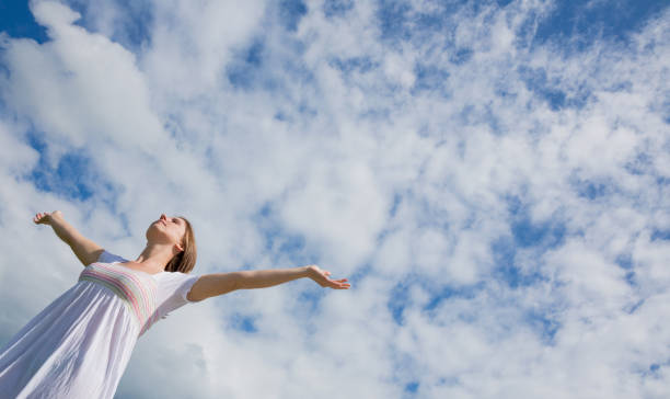 istock Woman with arms outstretched against blue sky and clouds 843932906