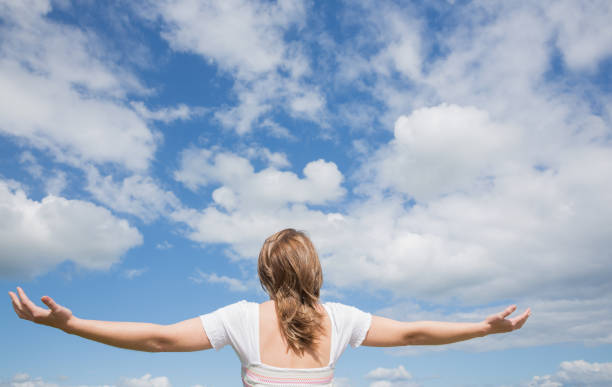 istock Woman with arms outstretched against blue sky and clouds 843932984