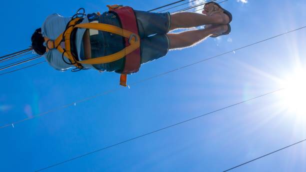 linea volo. una vista di un uomo che scivola su un cavo d'acciaio contro un cielo blu con nuvole bianche. riposo estremo e attivo. - women courage water floating on water foto e immagini stock