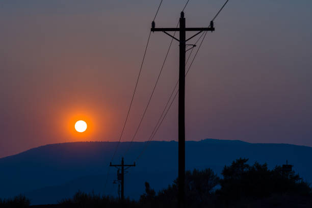 Silhouetted Powerlines and Poles with Mountains Sun - Scenic view of warm hazy sunset from fires burning off in distance.