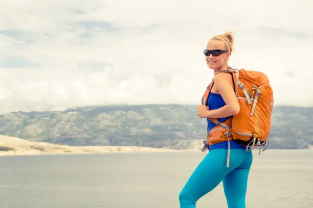 Woman hiker hiking with backpack, looking at sea and mountains view. Recreation and healthy lifestyle outdoors in summer nature. Beautiful inspirational landscape. Trekking and activity concept.