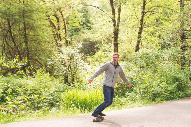 red-haired male skateboards through forest - hat trick imagens e fotografias de stock