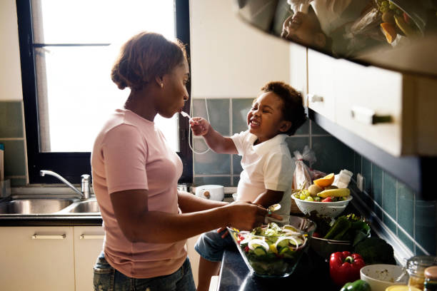 chico negro alimentación a madre con cocción de alimentos en la cocina - alimentar fotos fotografías e imágenes de stock