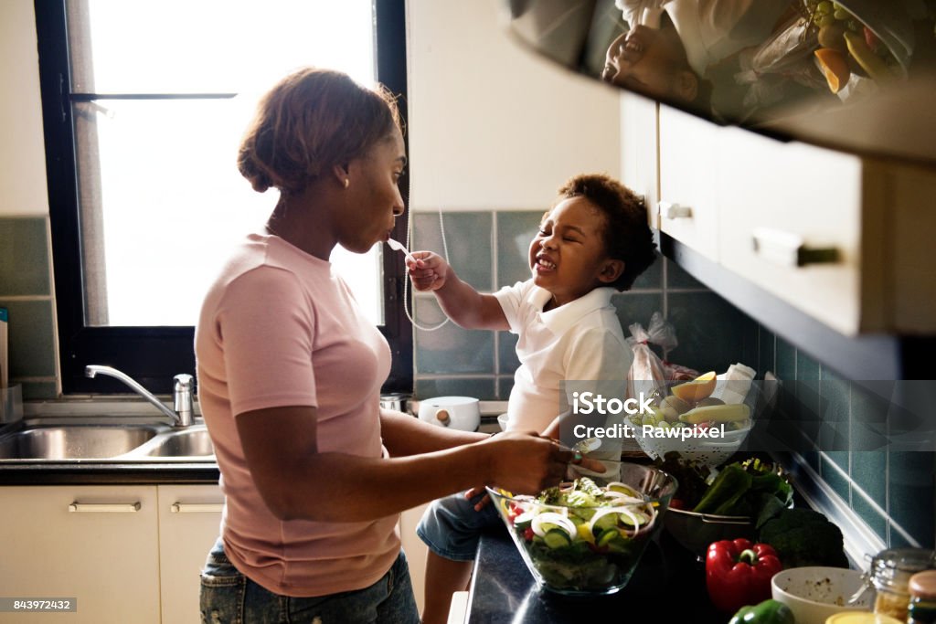 Black kid feeding mother with cooking food in the kitchen Family Stock Photo