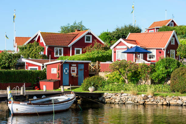 Coastal vacation cabins and boat Karlskrona: Travel documentary of the city surroundings. Red and white traditional coastal vacation cabins and moored boat in allotment area as seen from the sea. community garden sign stock pictures, royalty-free photos & images