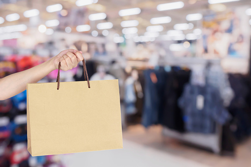 Woman hand hold shopping bag over clothing store in shopping mall defocused blur background with bokeh