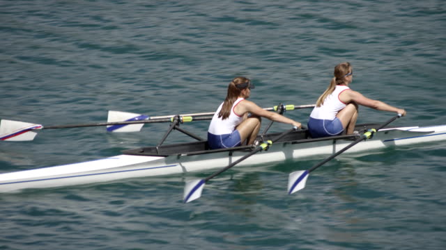 Female athletes sculling across a sunny lake in a double scull