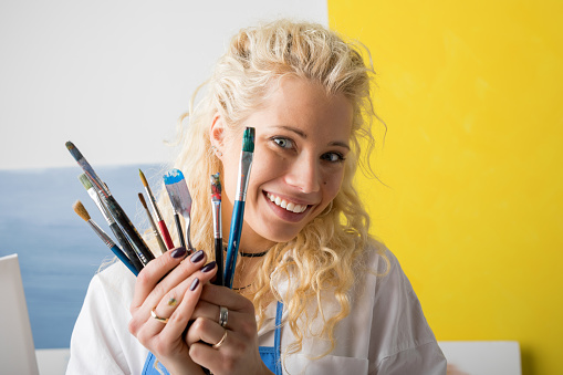 Artist in her studio holding paint brushes