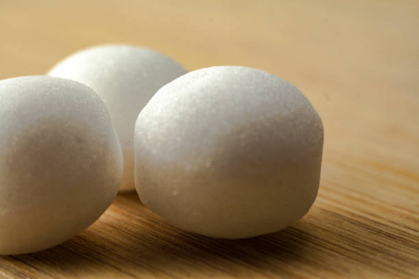Close-up of colourful sugar balls. The sugar balls roll out of a jar with a lid. White base in the foreground. Blurred balls in the background.