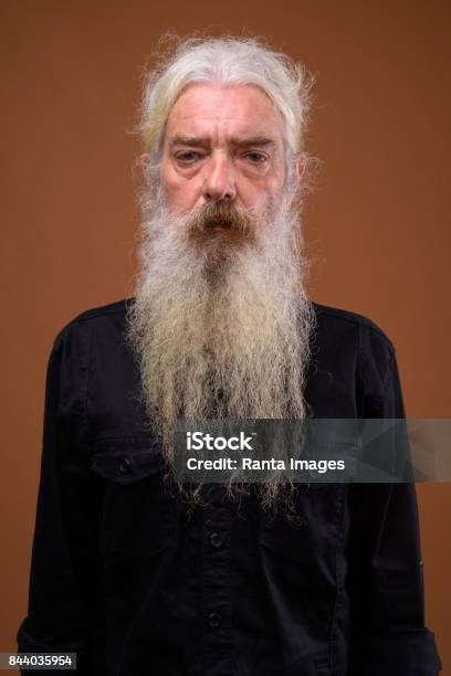 Disparo De Estudio De Senior Hombre Barbudo Con El Pelo Atado Hacia Atrás Contra Colores De Fondo Foto de stock y más banco de imágenes de Barba - Pelo facial